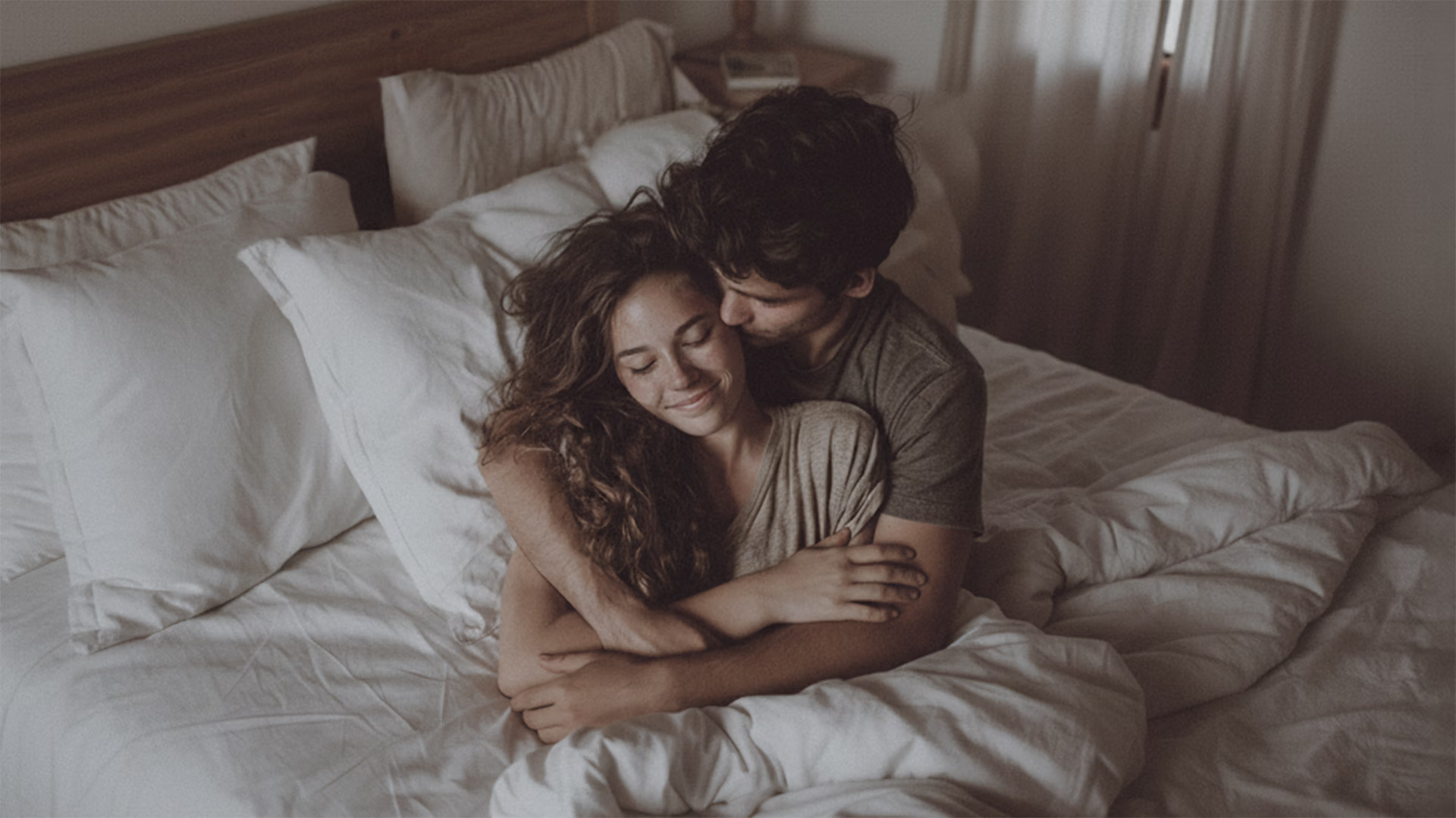 Pareja abrazada, calmada y sonriente, en la cama.