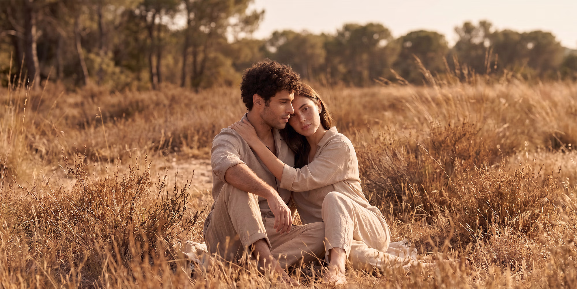 Pareja sentada en mitad del campo dándose un abrazo.